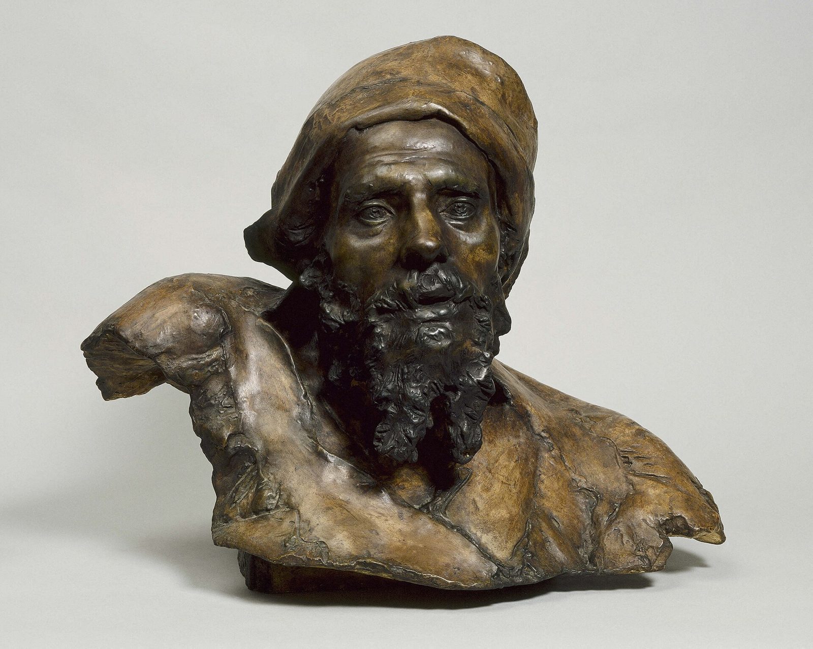 A patinated plaster bust of a bearded ragged man in a fur-trimmed hat, head lowered, eyes cast down, with a heavy, mournful expression